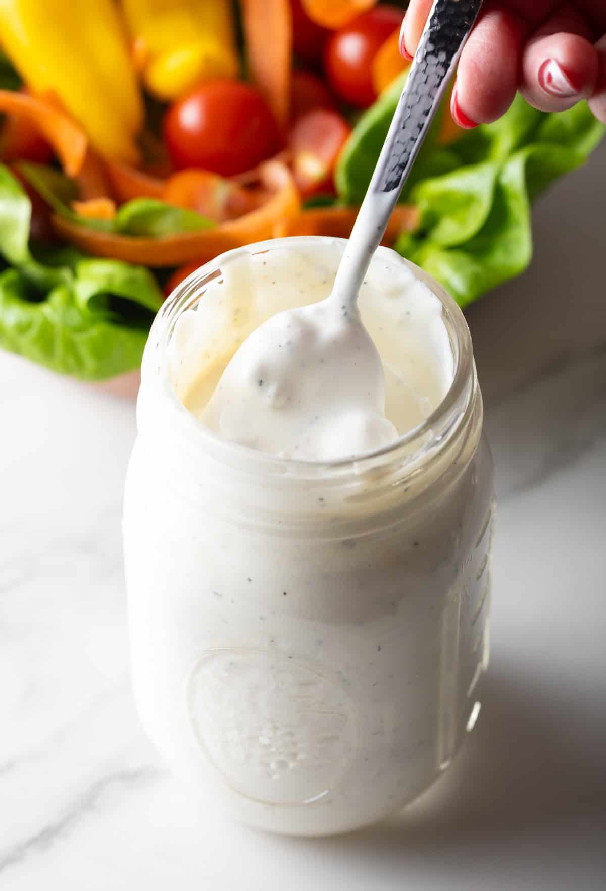 A spoon holding a serving of blue cheese dressing above a jar of the dressing.