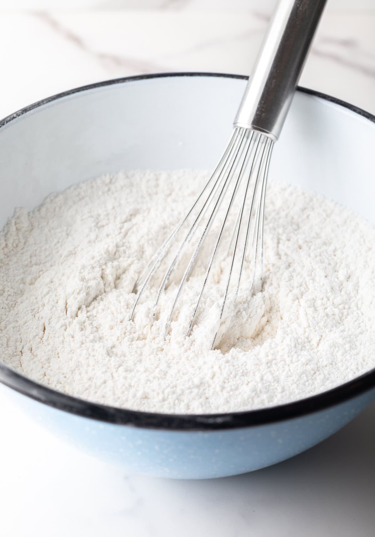 A bowl filled with a flour mixture is being mixed with a whisk.