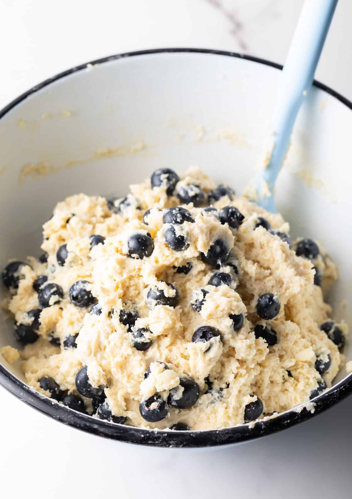 A blueberry biscuit dough is being mixed with a spatula in a mixing bowl.