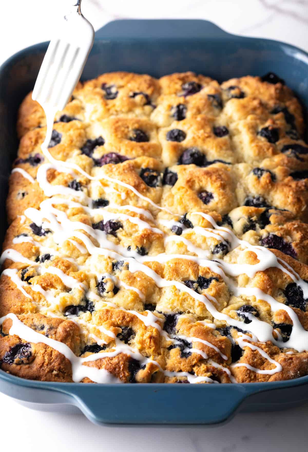 A tray of homemade blueberry biscuits with a fork drizzling lemon glaze over the top.