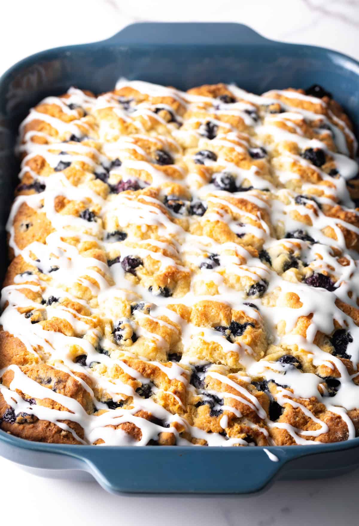 A blue baking dish filled with a lemon-glazed blueberry biscuit recipe.