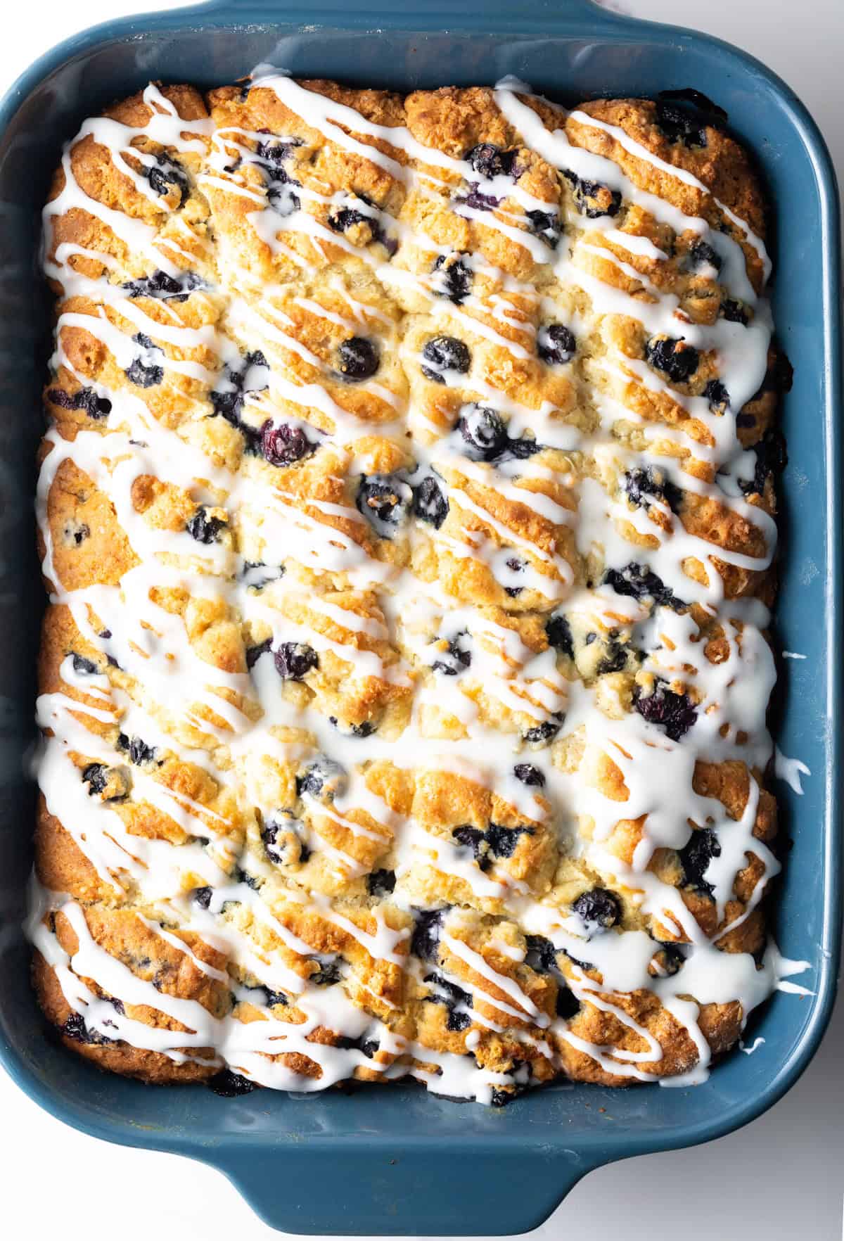 Top down view of a rectangle baking tray with blueberry biscuits and lemon glaze.