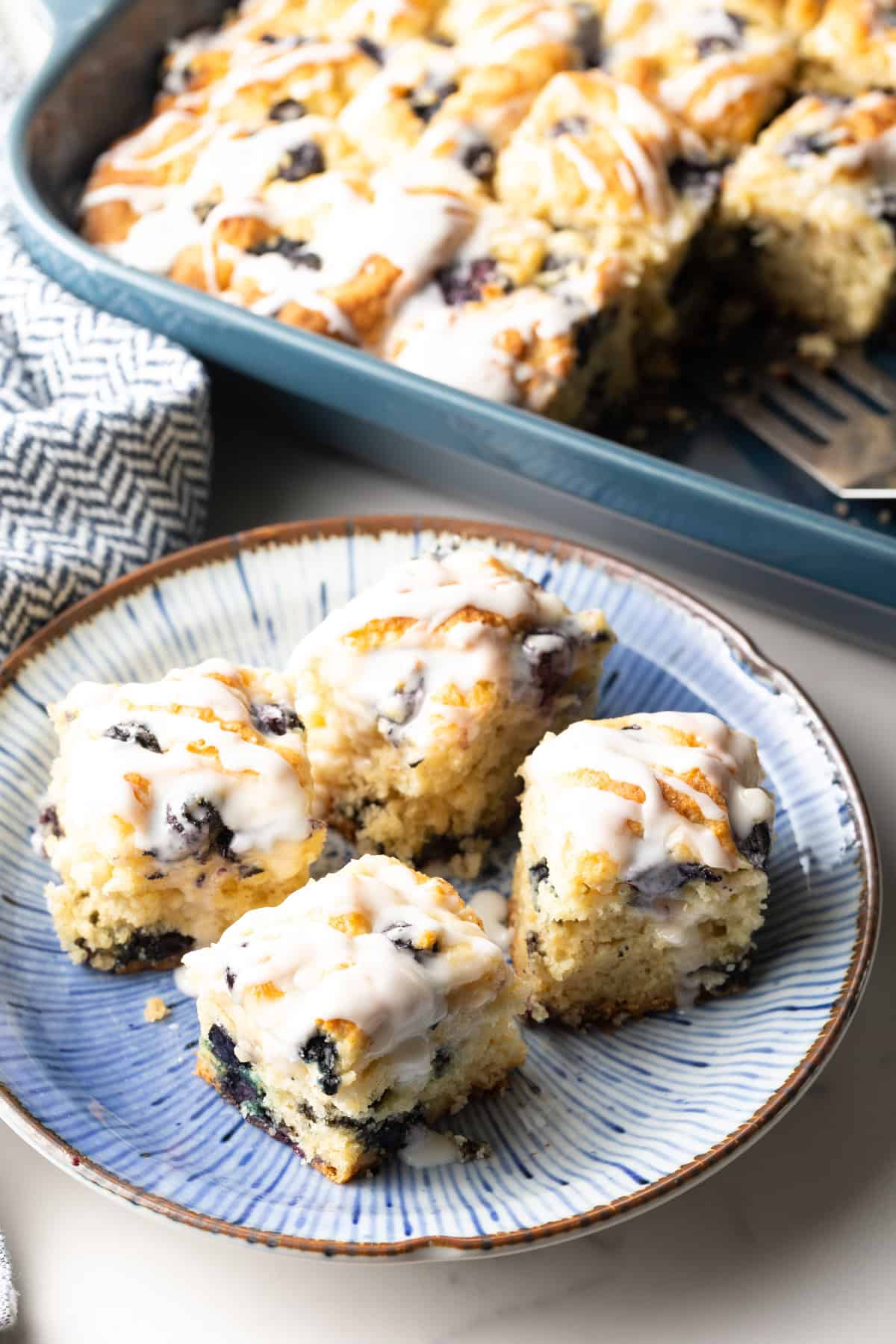 A blue plate with four homemade blueberry biscuits topped with lemon glaze.