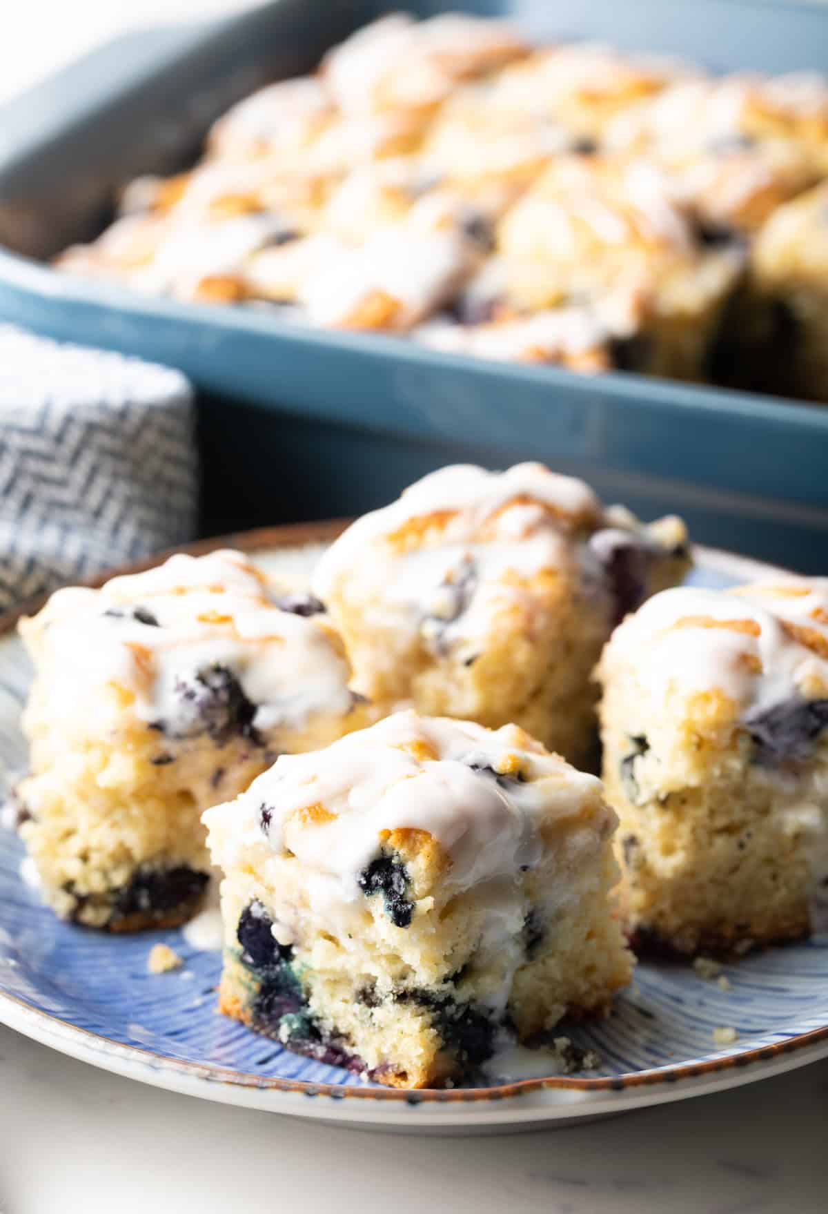 A blue plate with four homemade blueberry biscuits topped with lemon glaze.