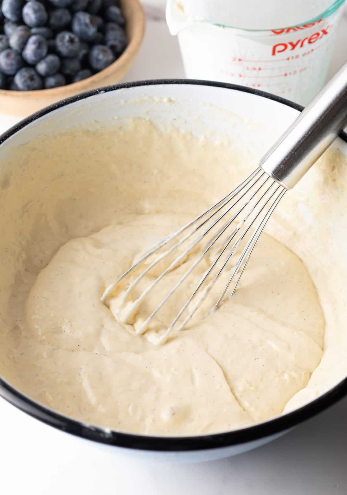 White bowl of pancake batter being stirred with a whisk.