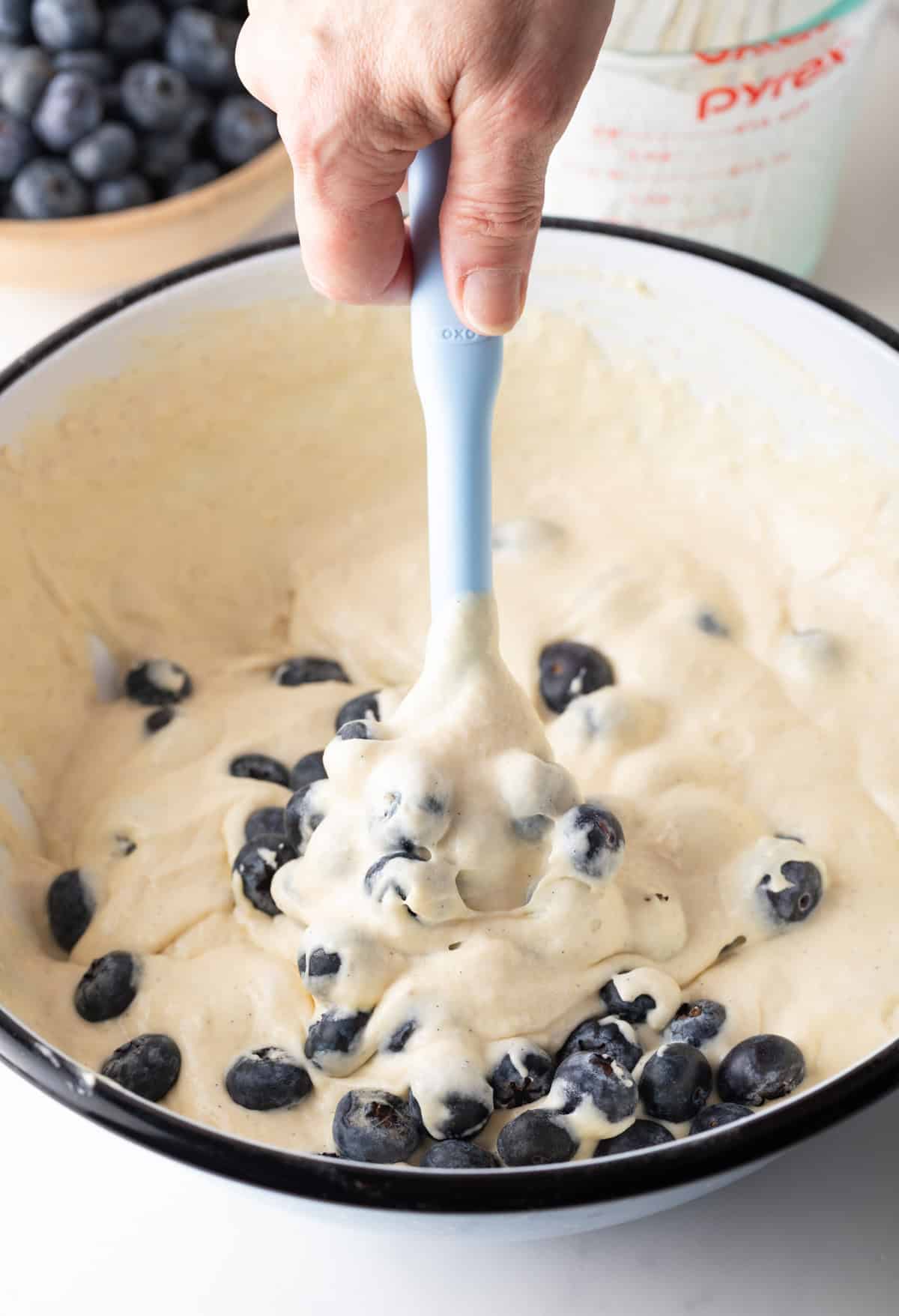 Using a light blue spatula to fold blueberries into the pancake batter.