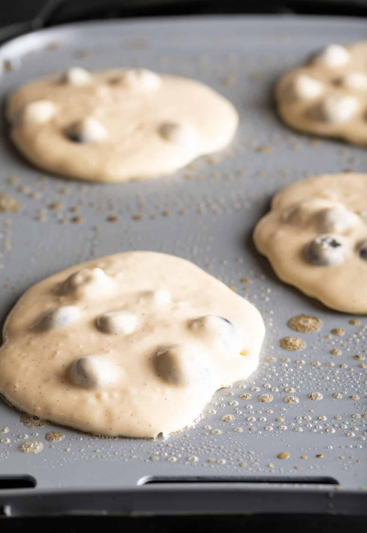 4 raw blueberry pancakes cooking on a griddle.