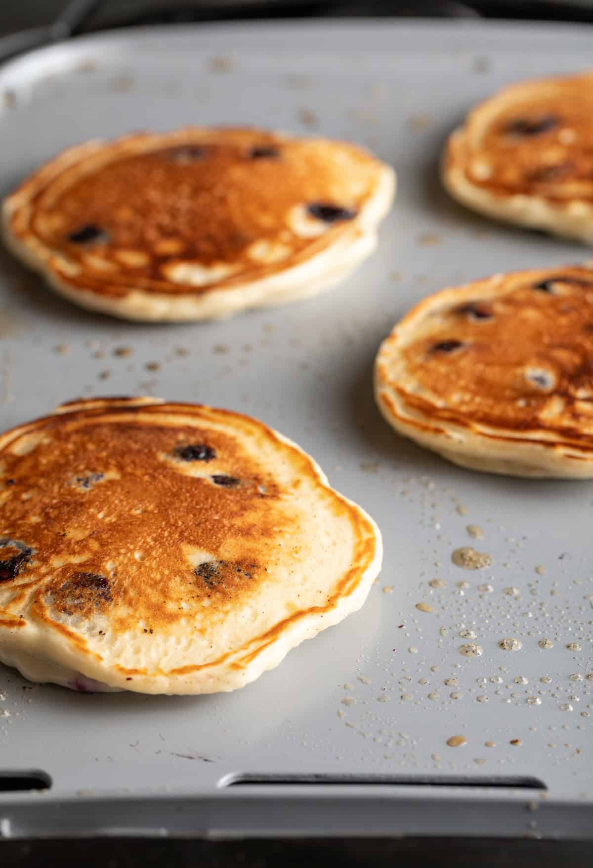 4 cooked blueberry pancakes on a griddle.