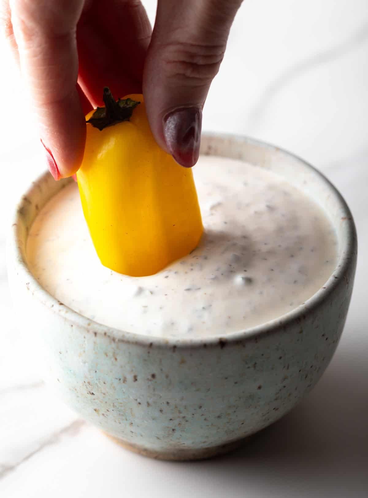 A yellow pepper is being dipped into a bowl filled with a homemade buttermilk ranch dressing recipe.