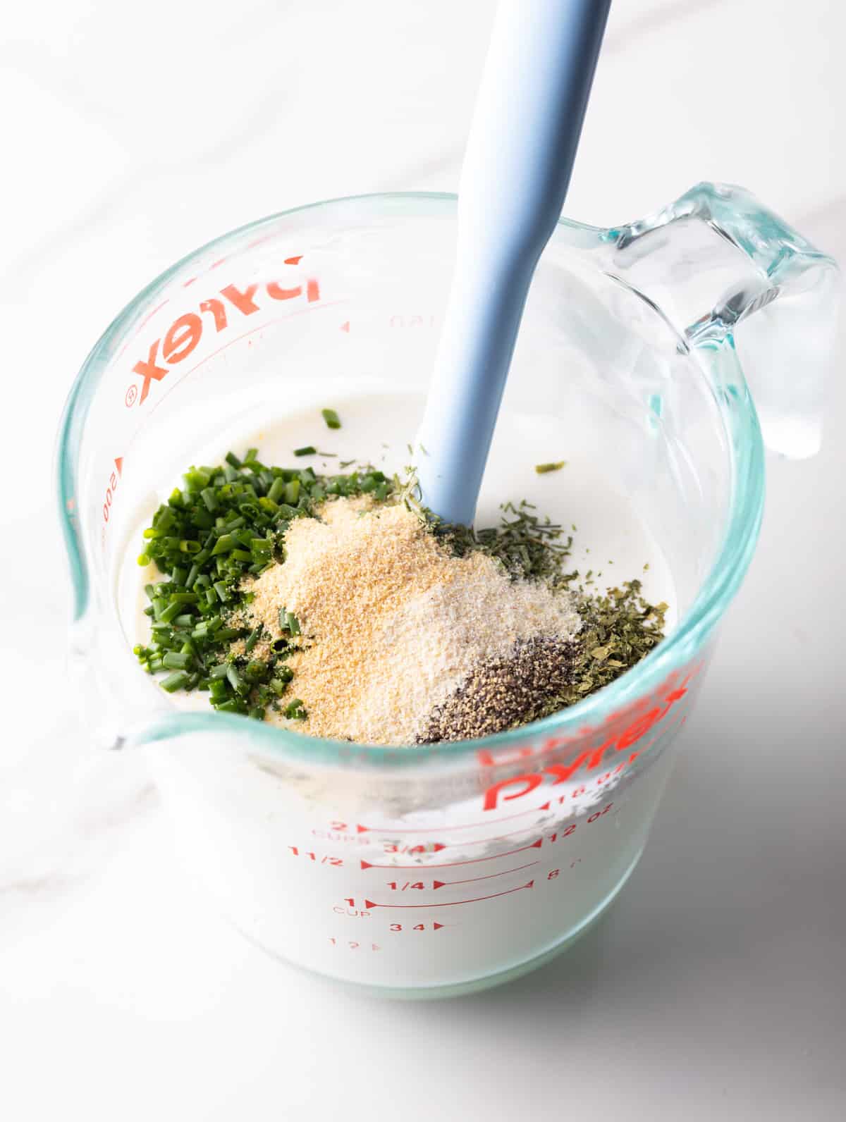 A buttermilk ranch dressing recipe is coming together in a glass measuring pitcher.