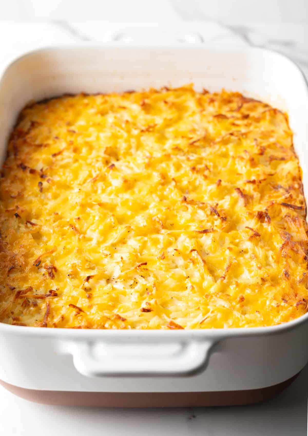 A cheesy hash brown casserole in a white baking dish, fresh from the oven.