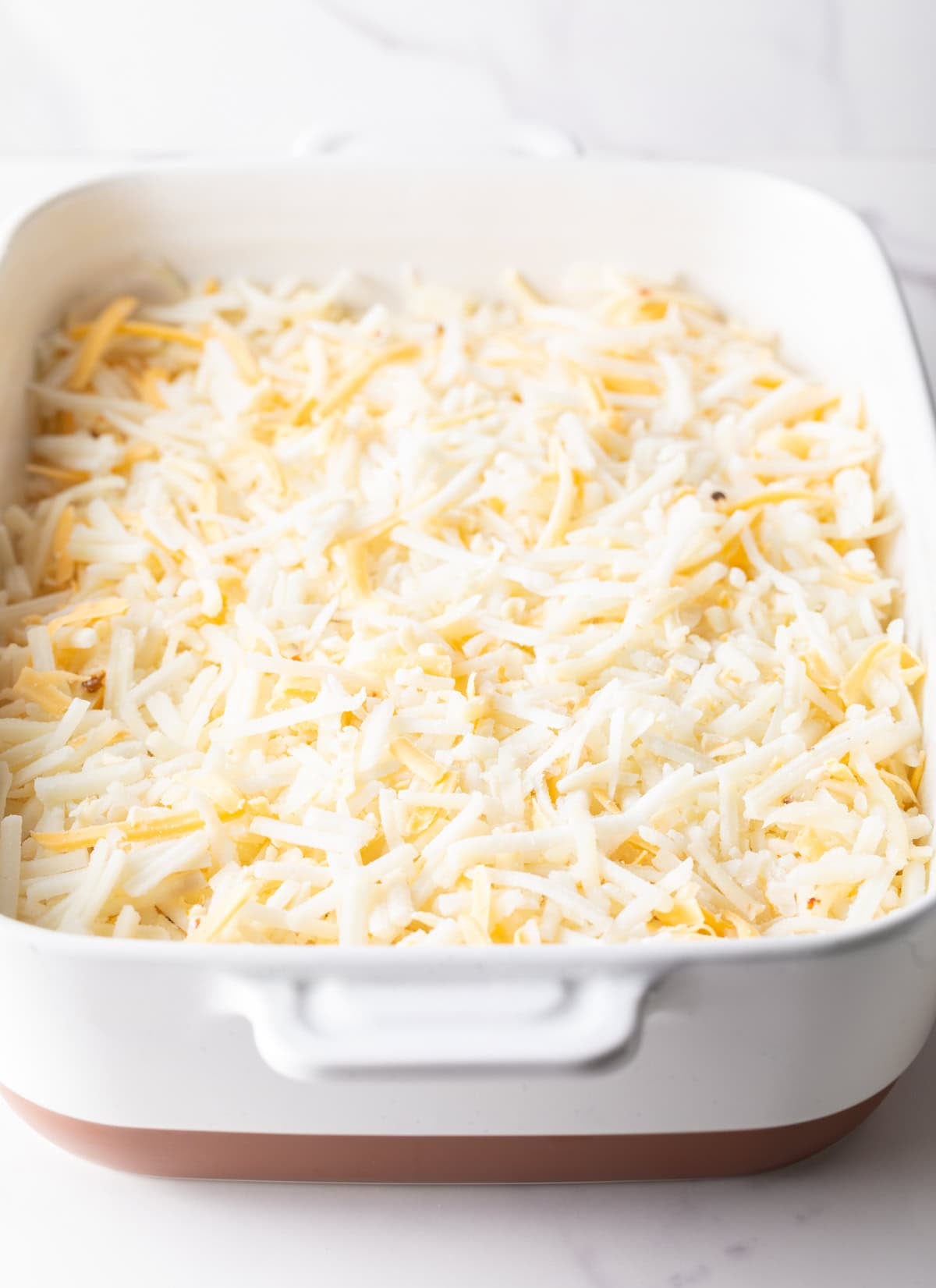 Shredded cheese is mixed with hash browns in a white baking dish.