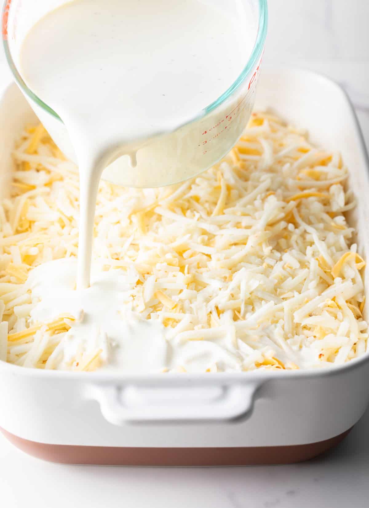 A cream mixture is being poured over cheesy hashbrowns.