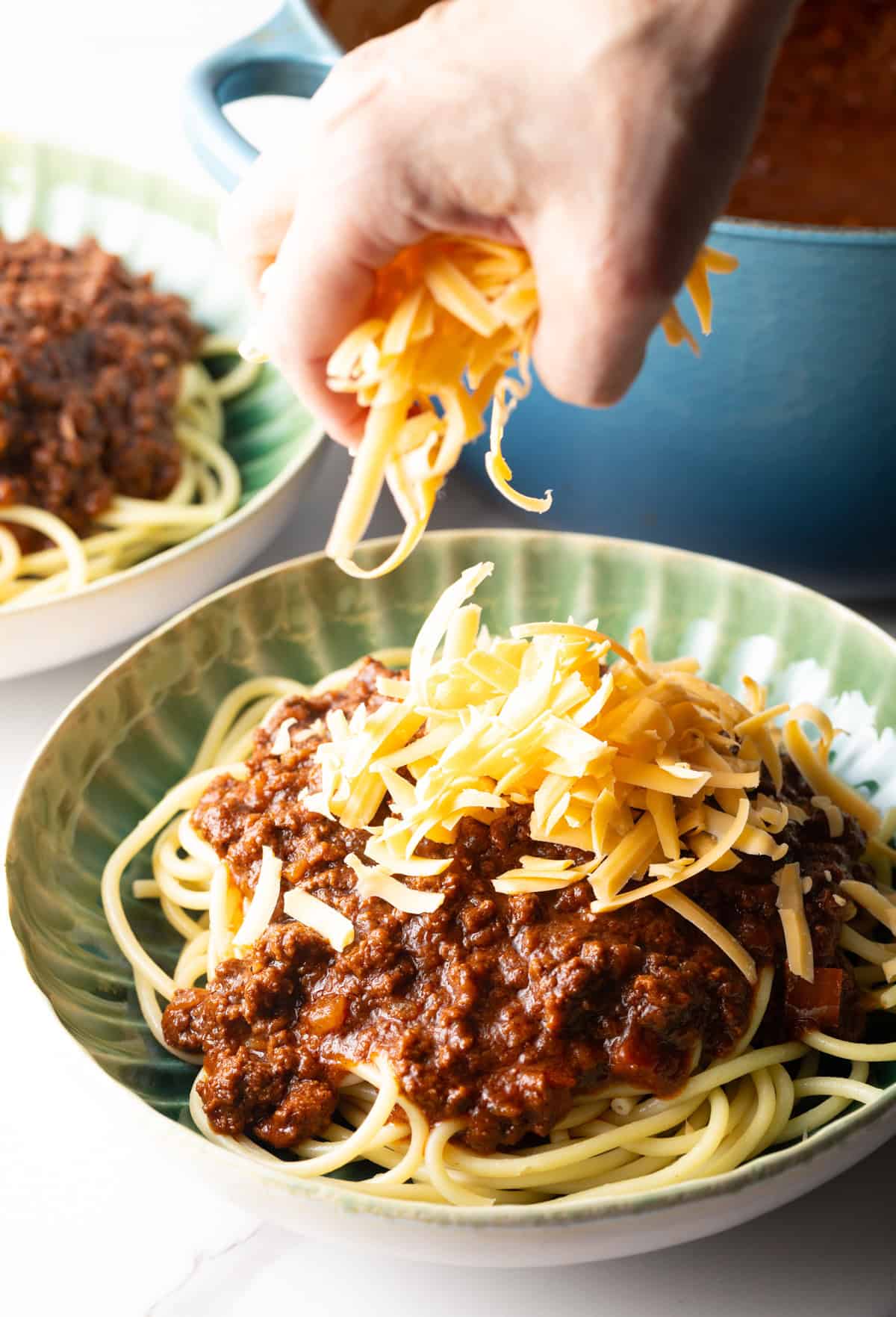 A hand is topping skyline chili with shredded cheese.