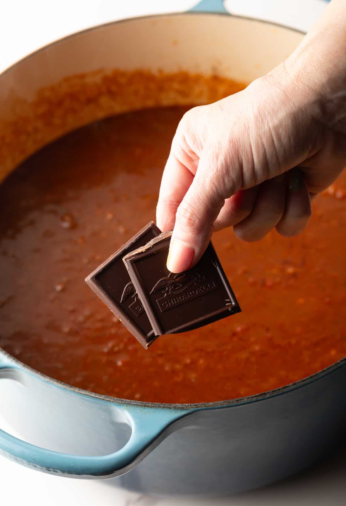 Chocolate is being added to a Cincinnati chili mixture in a pot.