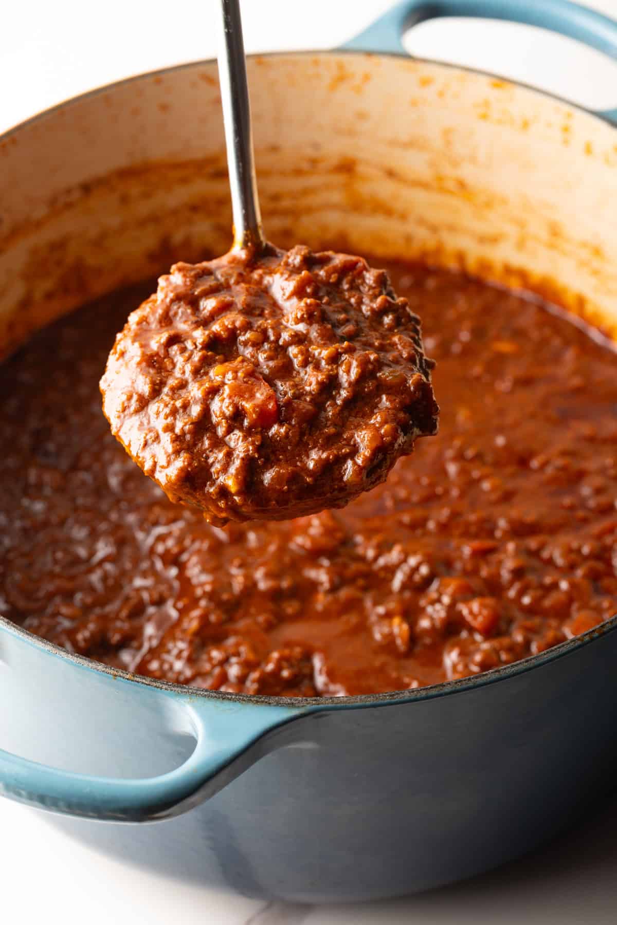 A scoop of skyline chili is being held above a pot full of the Cincinnati chili.