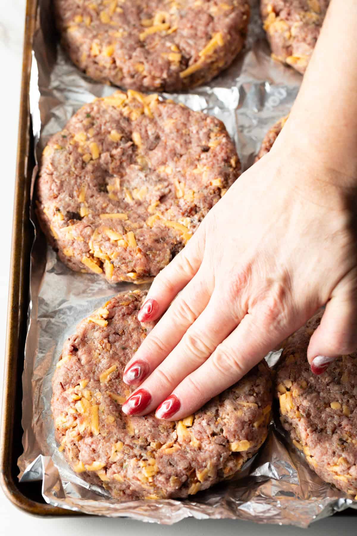 A hand is pressing on a crack burger patty to form its shape.