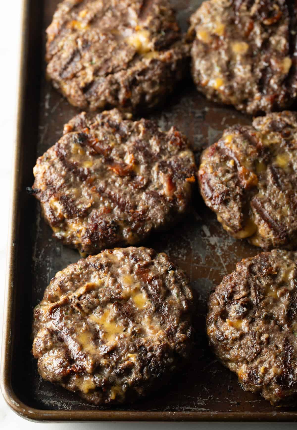 Grilled crack burger patties are sitting on a black baking tray.