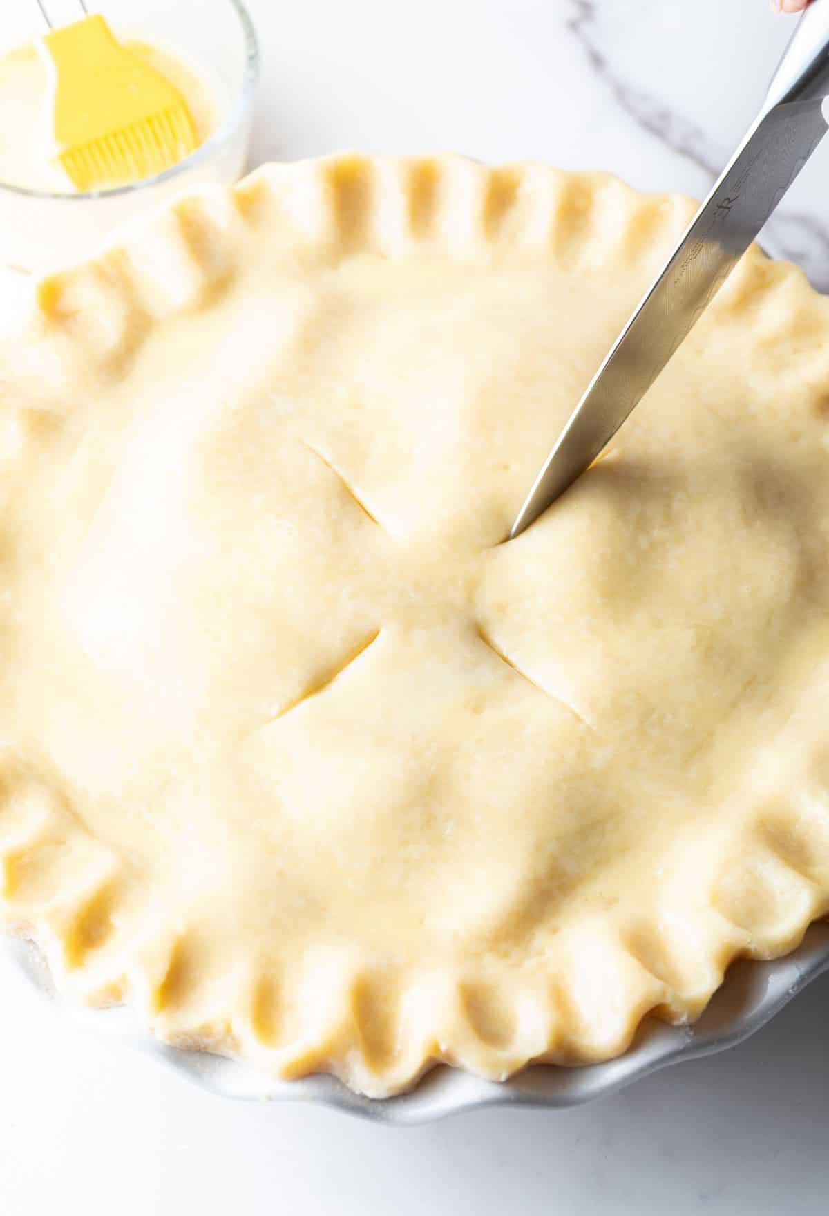 Venting slits are being cut into the top crust of an apple pie recipe.