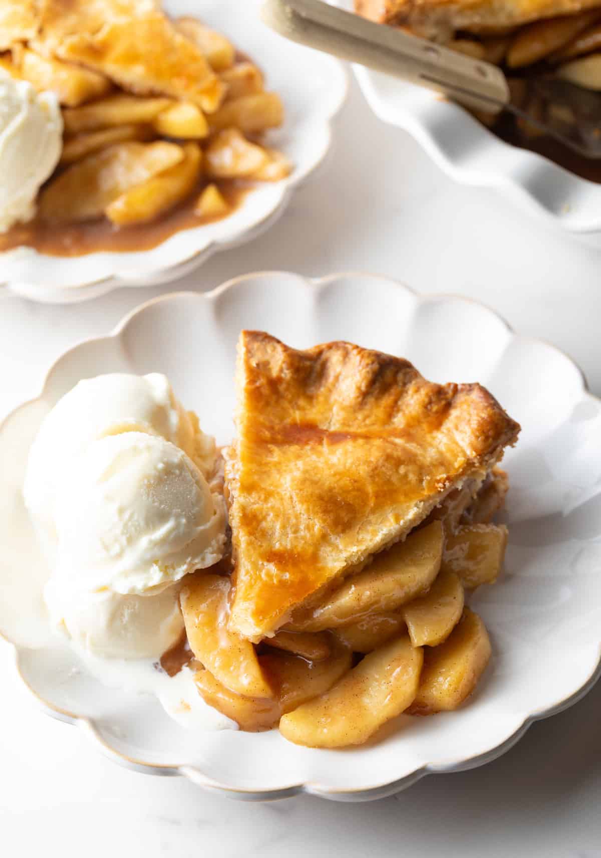 A slice of pie from an easy apple pie recipe is sitting on a white plate next to vanilla ice cream.