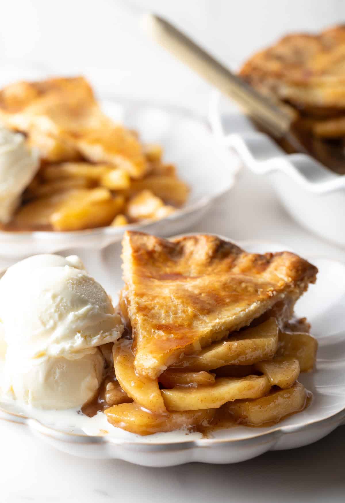 A slice of pie from an easy apple pie recipe is sitting on a white plate next to vanilla ice cream.