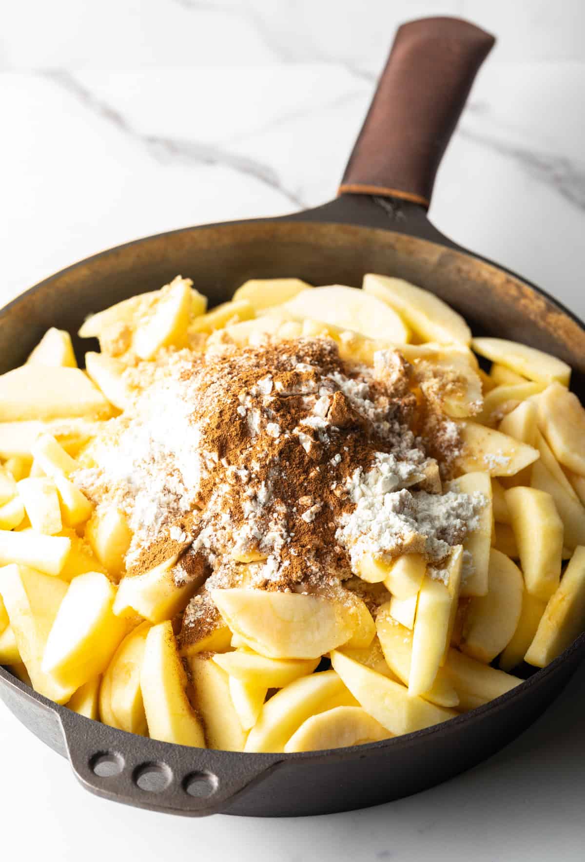 Apple slices in a black skillet topped with a cinnamon and sugar mixture.