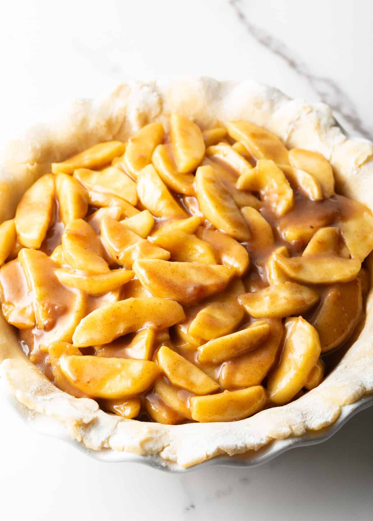 Homemade apple pie filling is sitting on top of an unbaked pie crust.