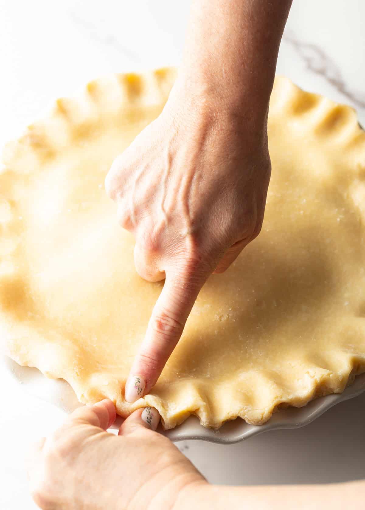 A hand is preparing pie crust in a pie plate, ready for the apple filling.