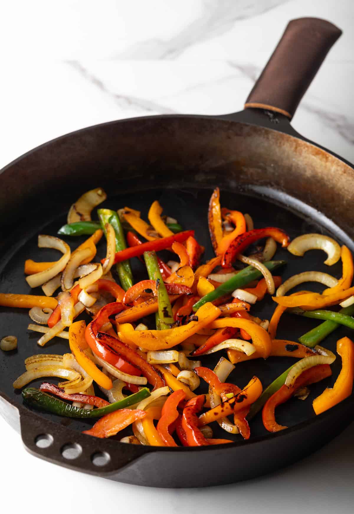 Bell peppers and onions are being sautéed in a black skillet.
