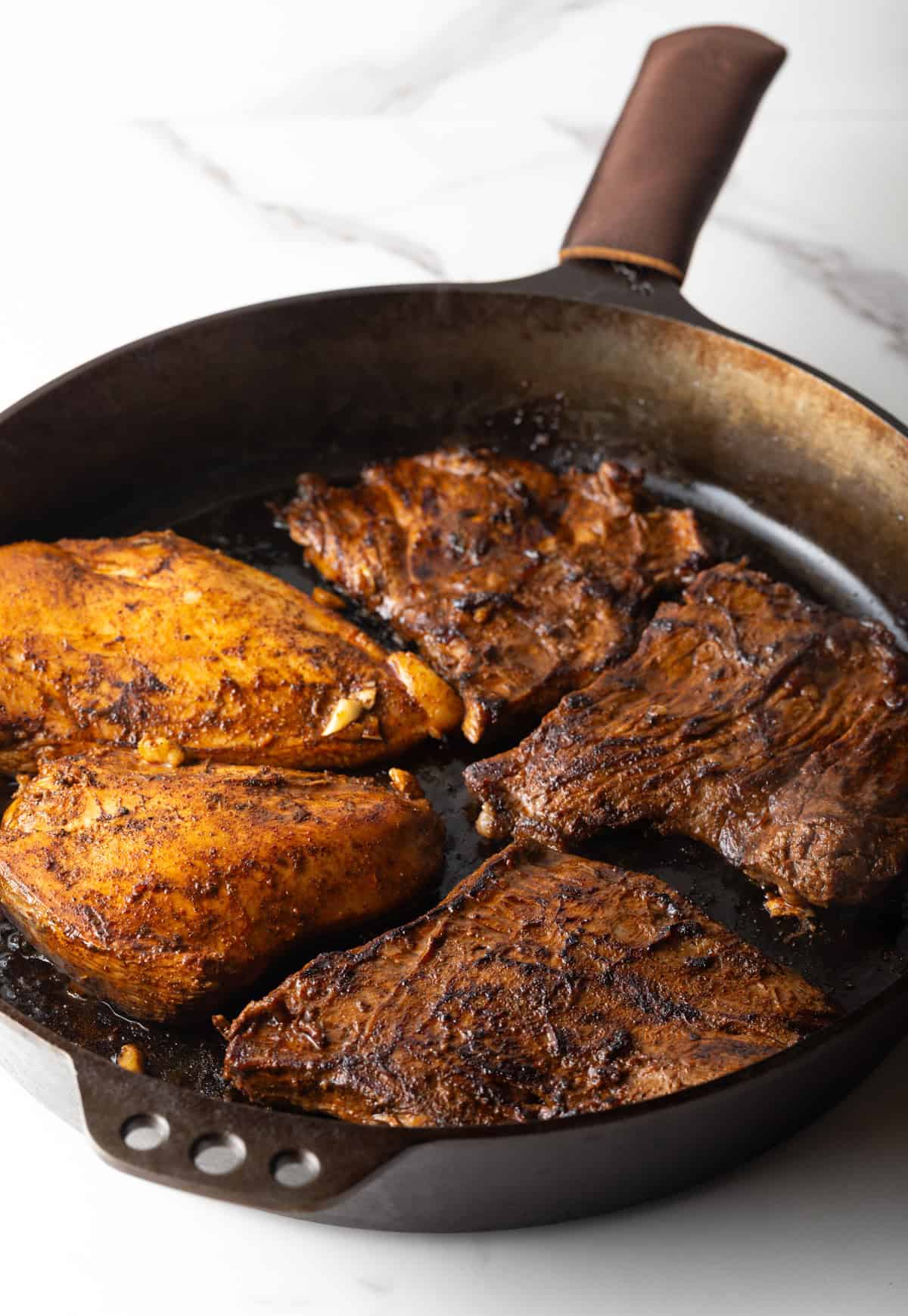 Five steaks are being seared in a black skillet.