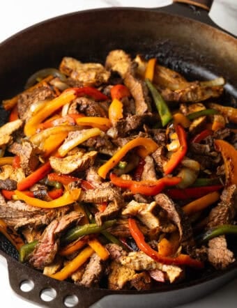 A black skillet filled with steak and pepper fajitas using a homemade fajita marinade.
