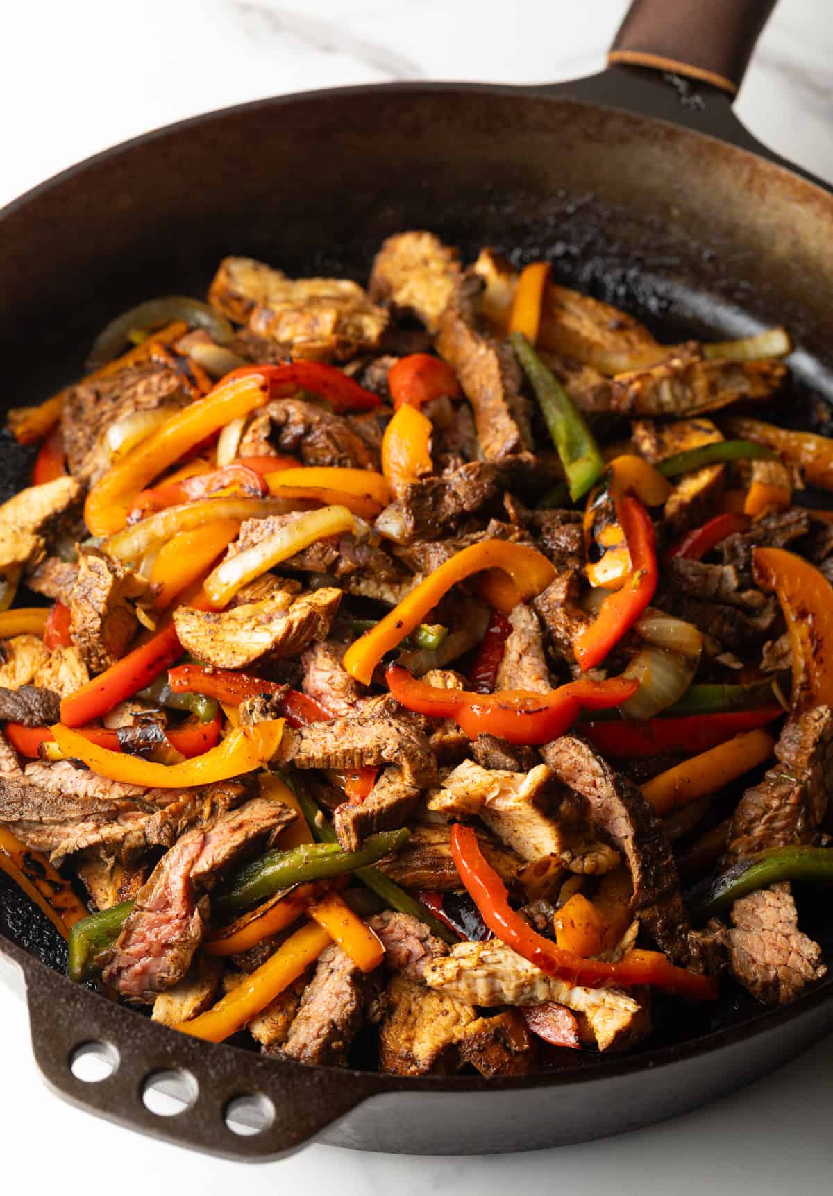 A black skillet filled with chicken and peppers fajitas using a homemade fajita marinade.
