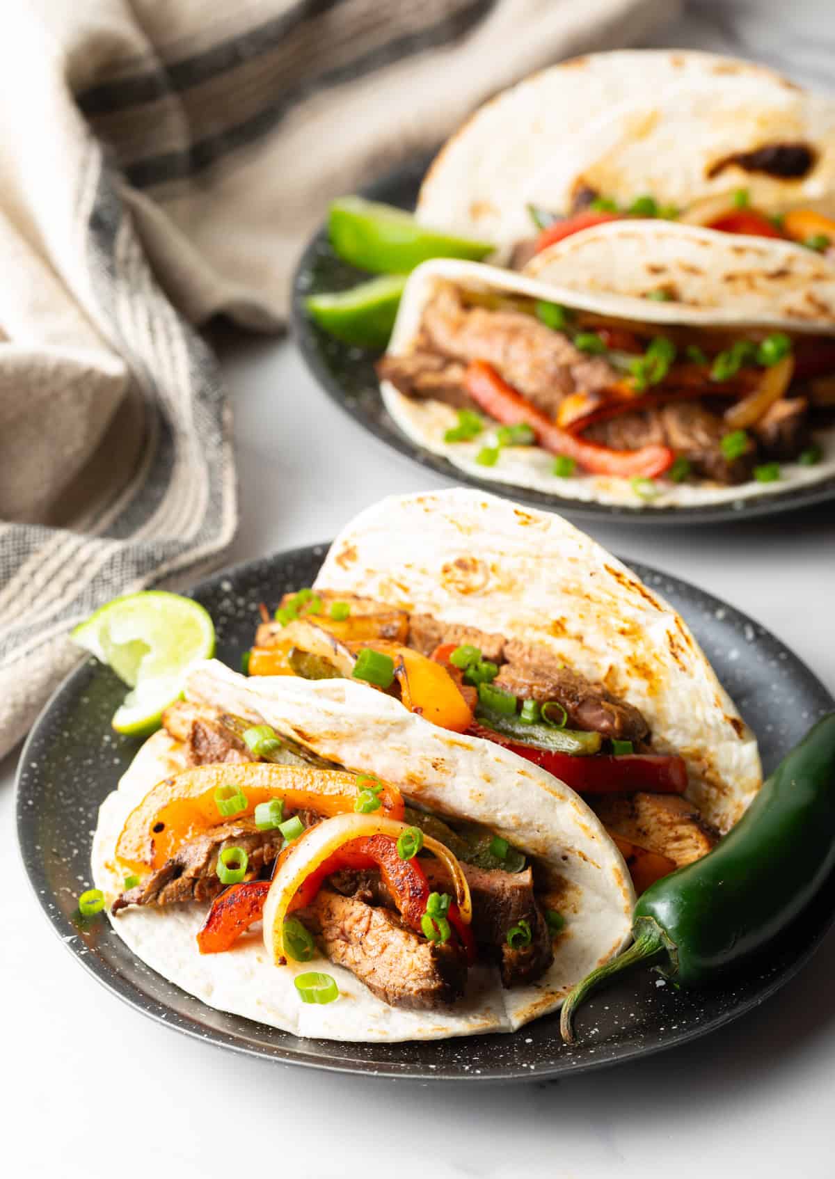 Two tacos on a plate filled with a steak fajita mixture using a steak fajita marinade.
