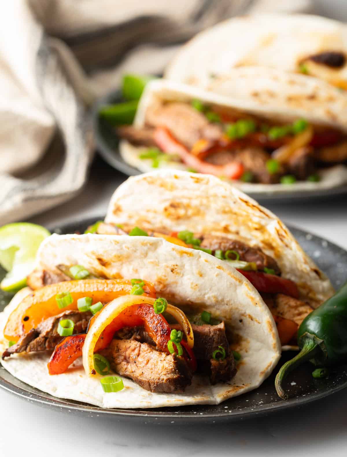 Two steak fajitas in tortillas, sitting on a black plate.