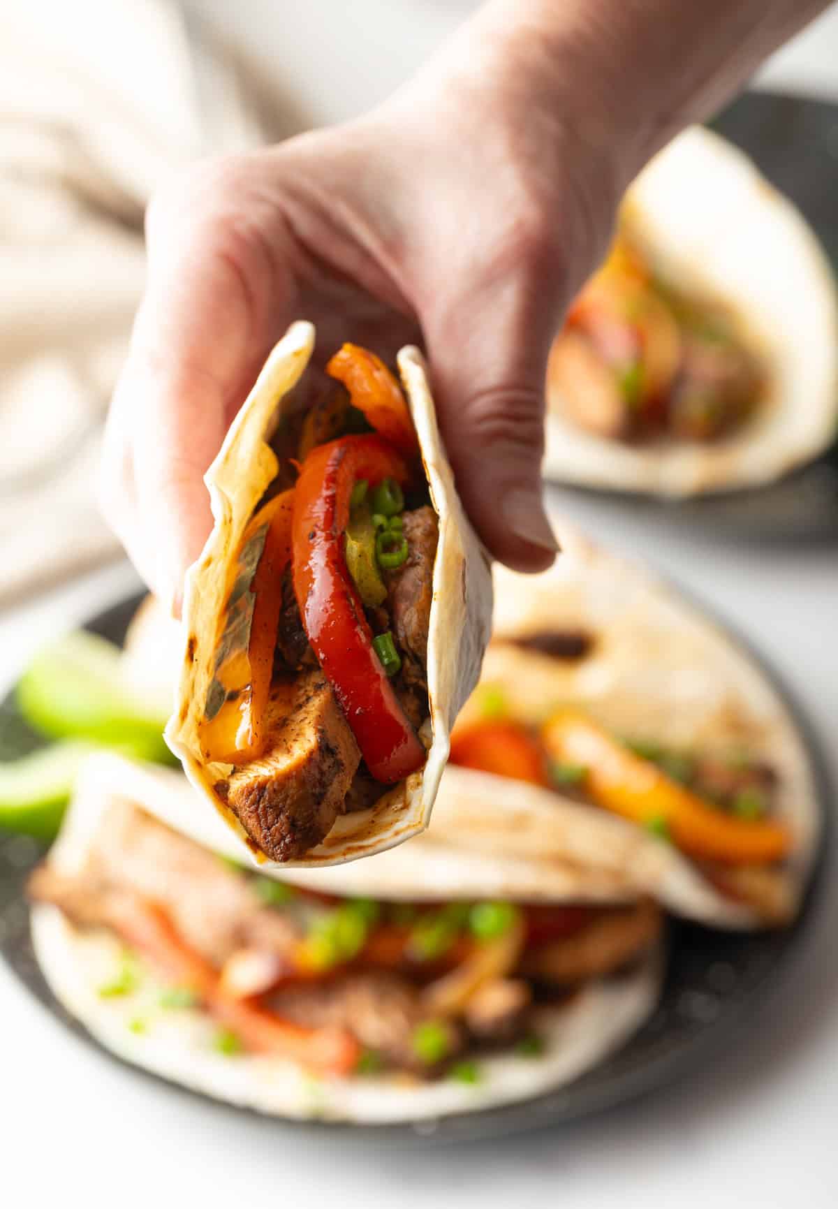 A hand holding a tortilla filled with a homemade steak fajita recipe.