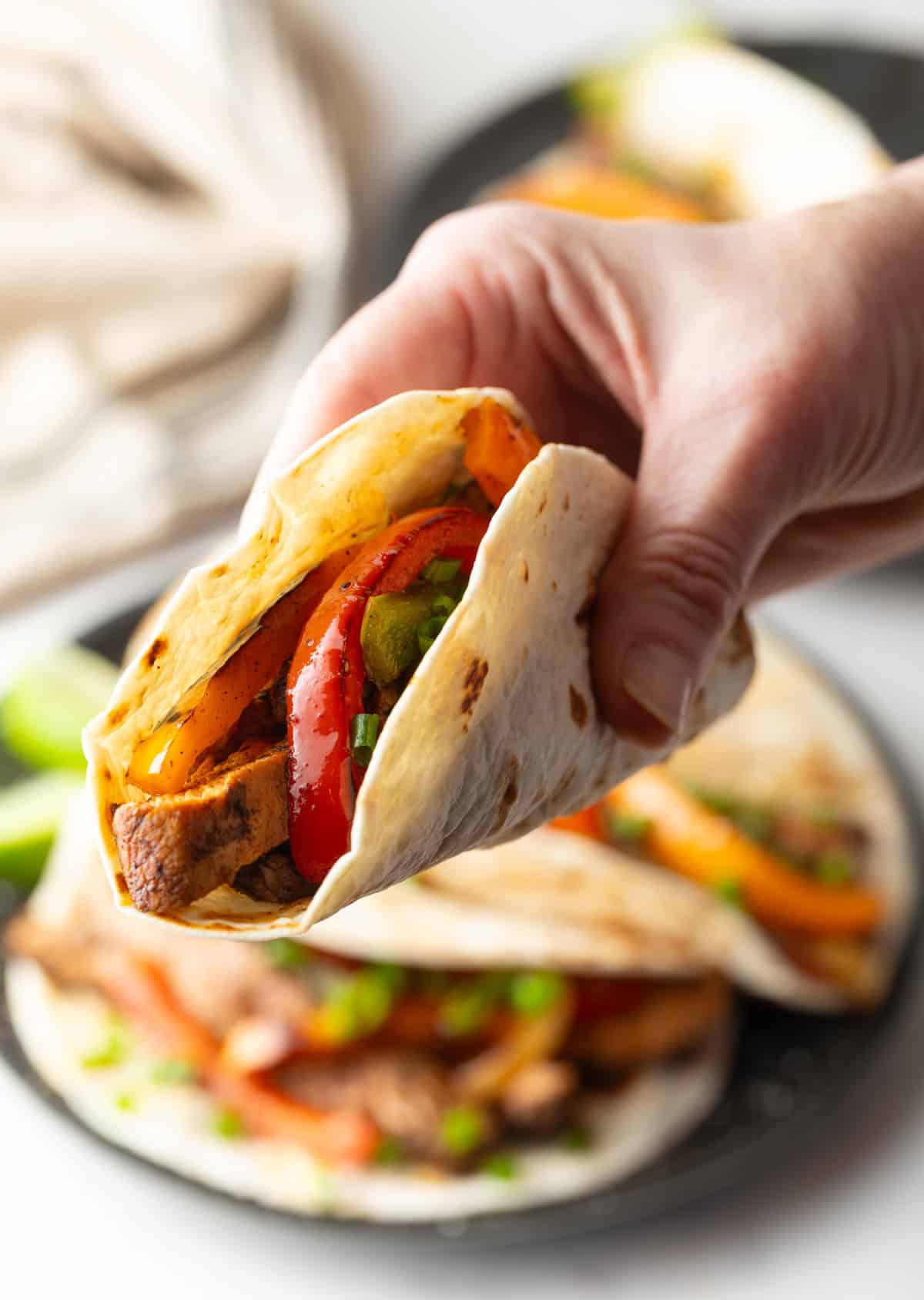 A hand holding a tortilla filled with a homemade chicken fajita mixture.