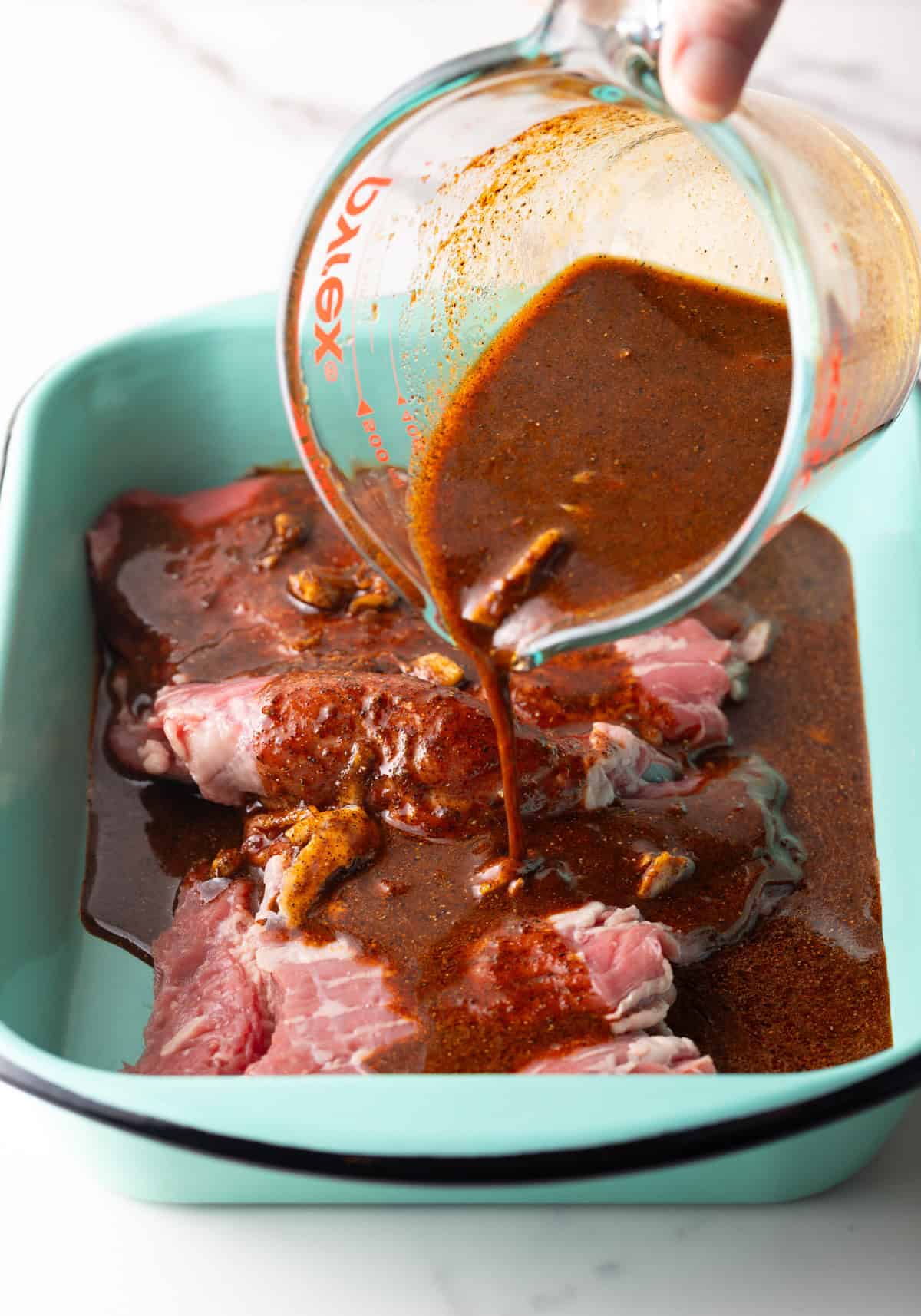 An easy homemade fajita marinade is being poured over steak in a blue baking pan.