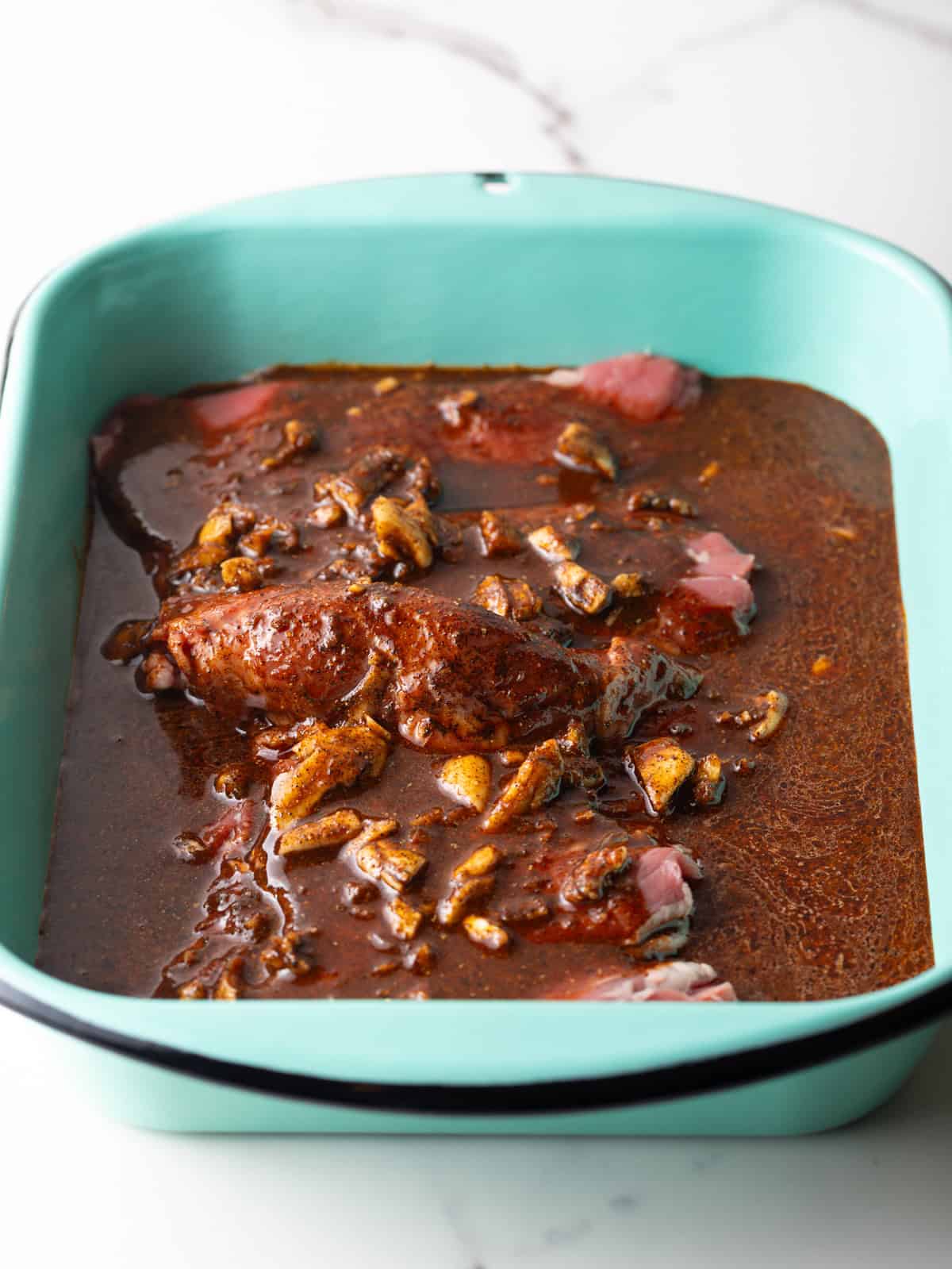 A blue baking dish filled with steak submerged in a fajita marinade.