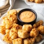 A white plate filled with fried fish nuggets next to a ramekin of dipping sauce.
