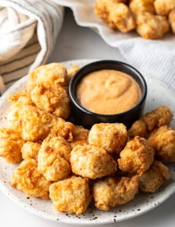 A white plate filled with fried fish nuggets next to a ramekin of dipping sauce.