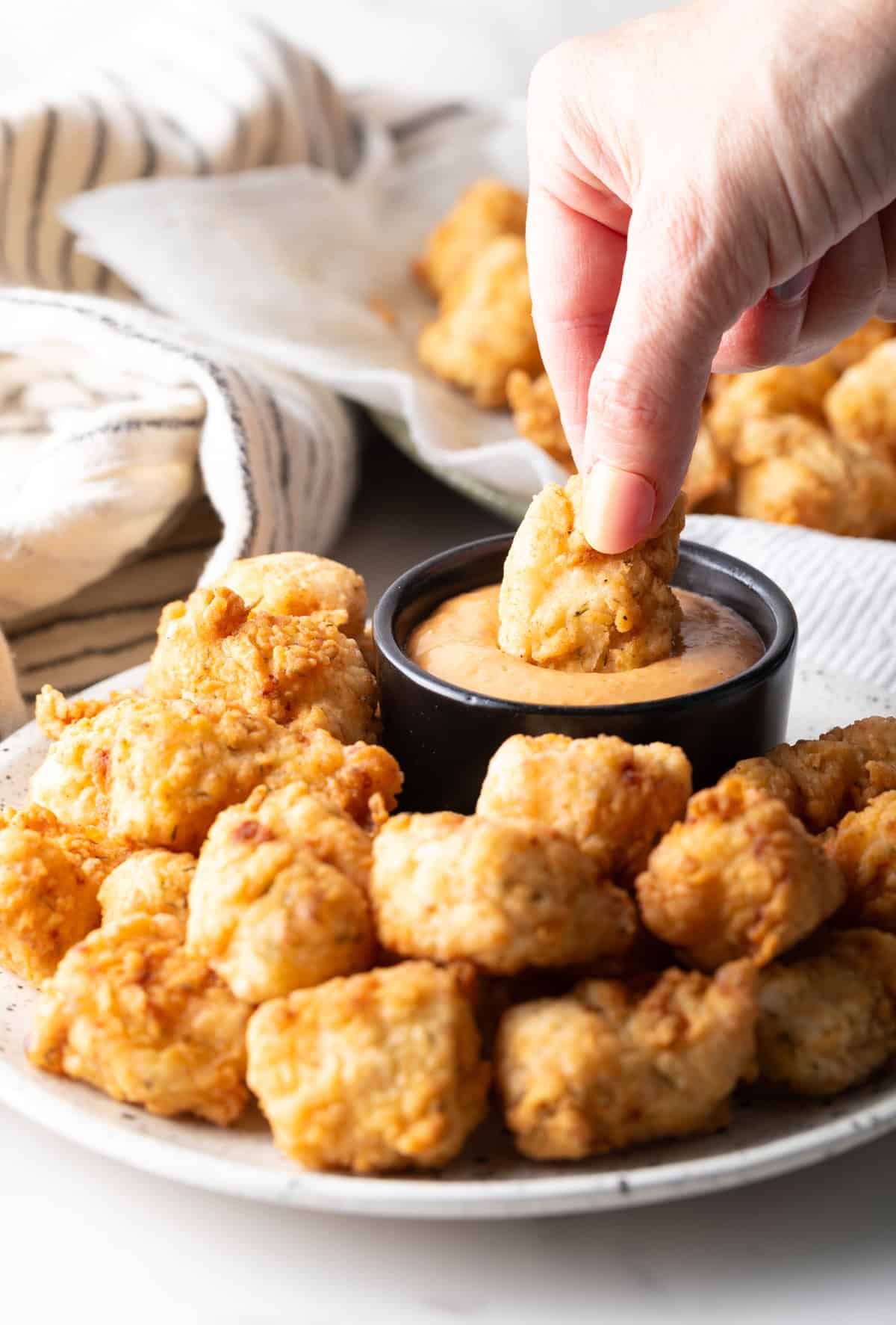 A hand is dunking a homemade fish nugget into a ramekin of sauce.