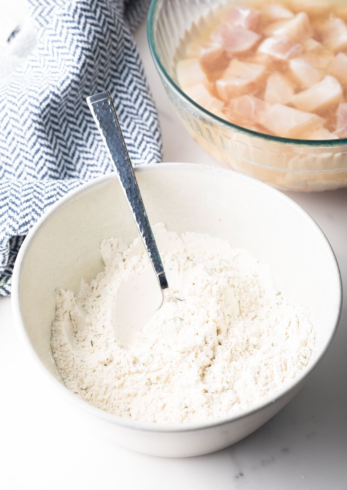 A white bowl filled with a flour mixture for frying fish bites.
