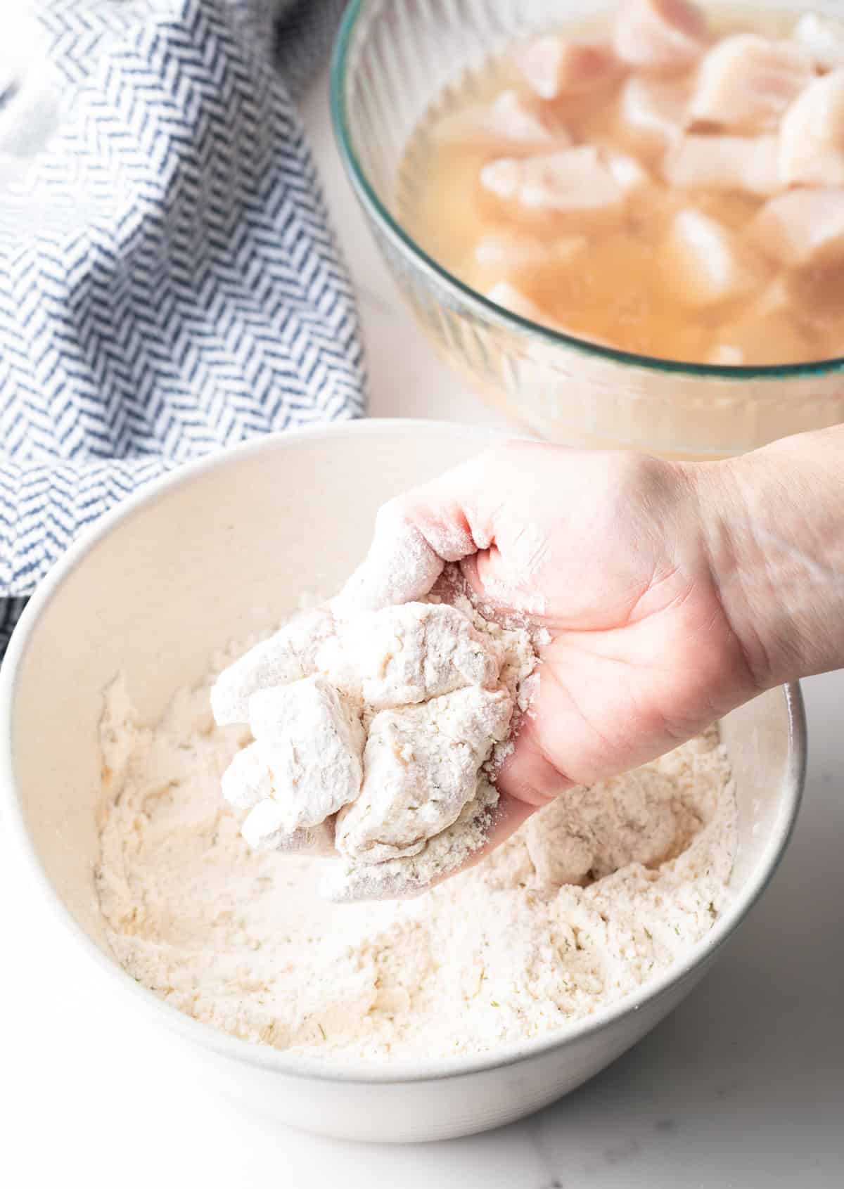 A hand is tossing raw fish nuggets in a flour mixture for frying.