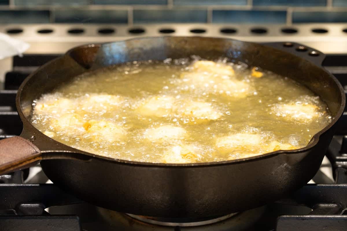 Fish nuggets are being fried in oil in a black skillet.