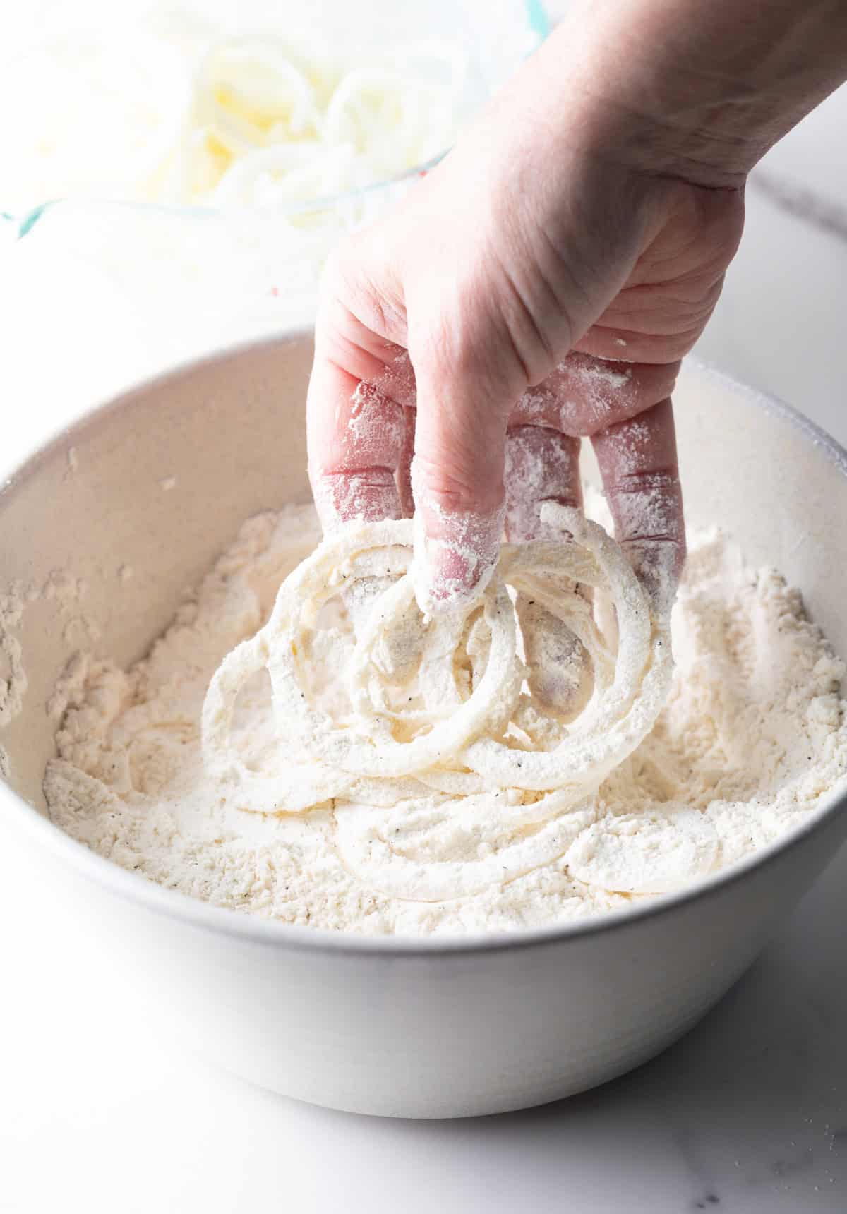 Thinly sliced onions are being coated in a flour mixture for a homemade French's fried onions recipe.