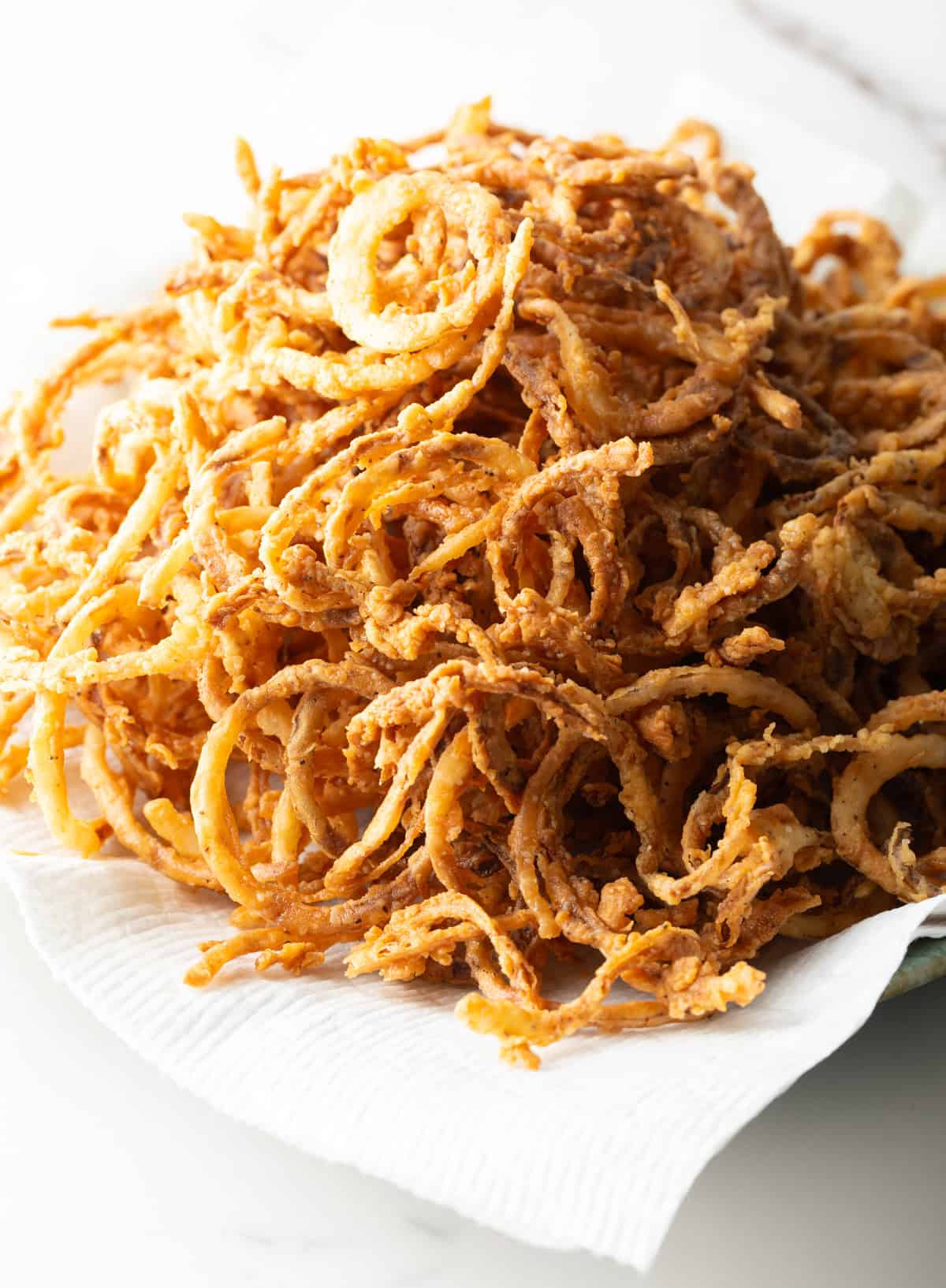 A batch of a crispy French fried onions recipe on a paper towel-lined plate.