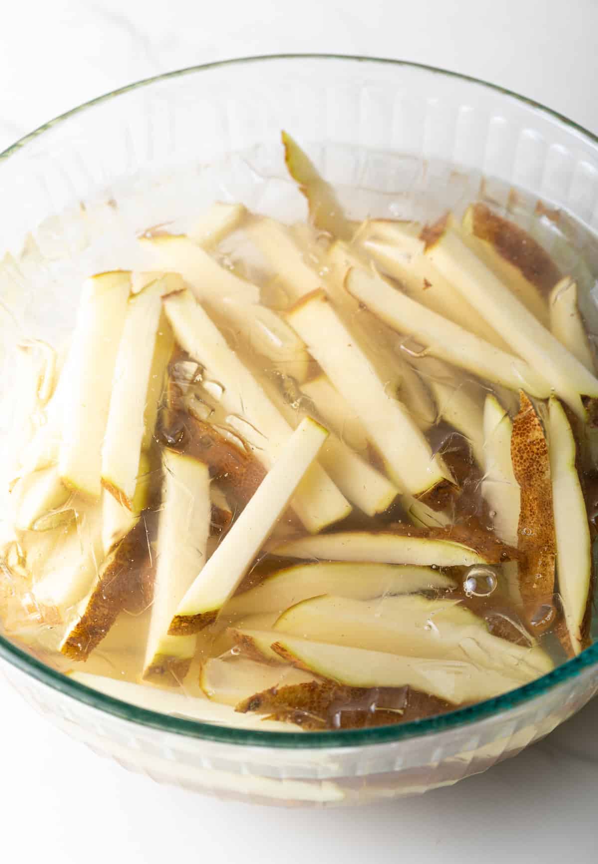 Raw potato slices are sitting in a bowl of ice water.