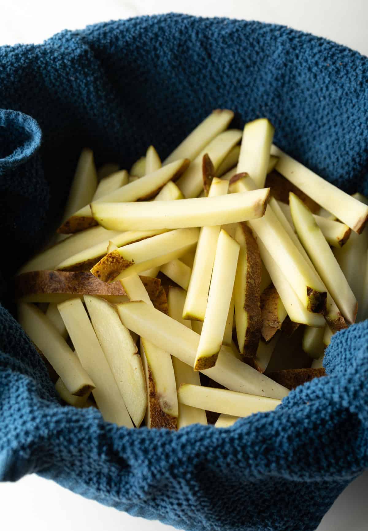 Raw potato slices are drying off in a towel-lined bowl.