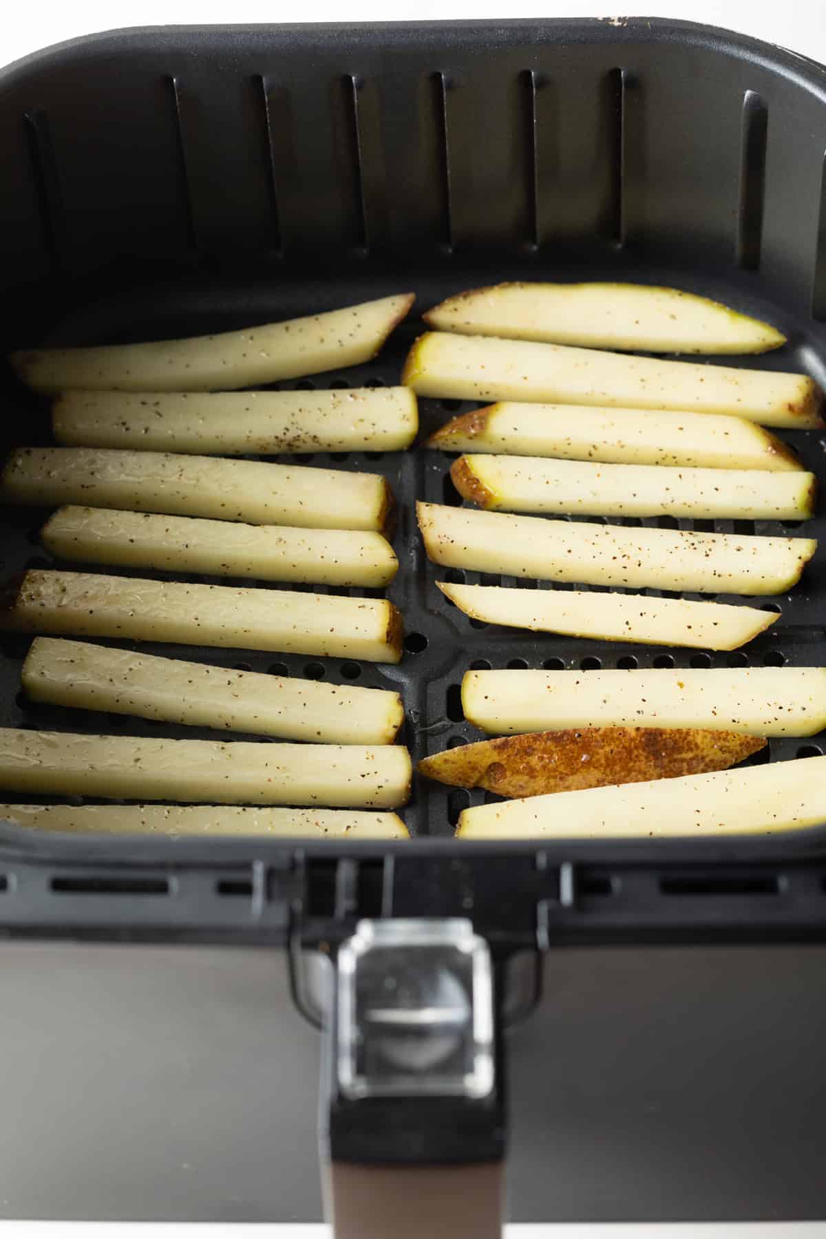 A single layer of potato slices lined up in an air fryer basket.