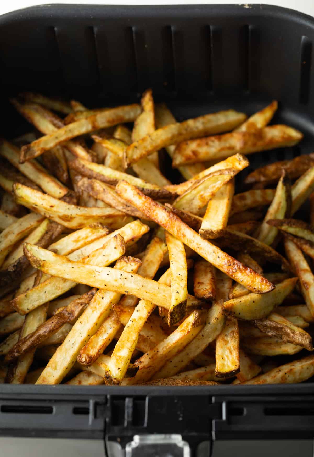 A batch of crispy air fryer fries sitting in an air fryer basket.